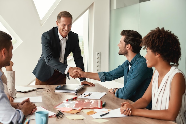 Photo celebrating success two cheerful colleagues shaking hands and smiling while sitting in the modern