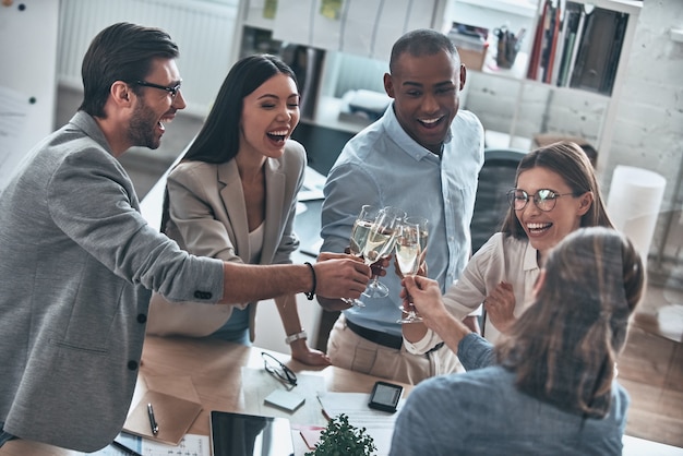 Celebrating. Top view of young business people toasting each other and smiling while standing in the board room