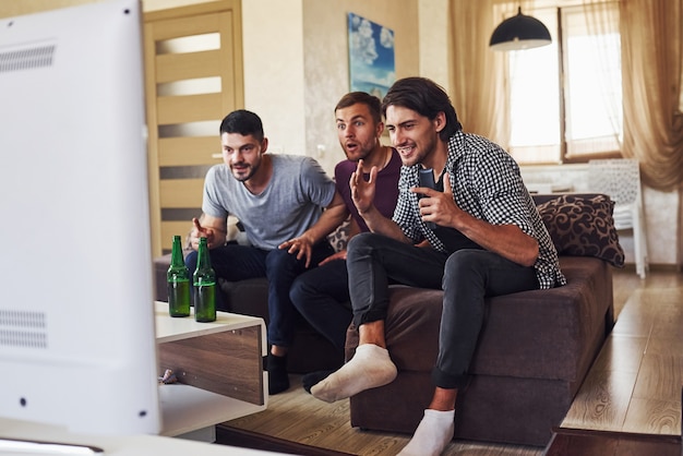 Celebrating victory. Excited three friends watching soccer on TV at home together.