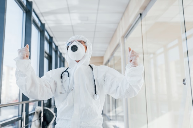 Celebrating victory. Female doctor scientist in lab coat, defensive eyewear and mask standing indoors