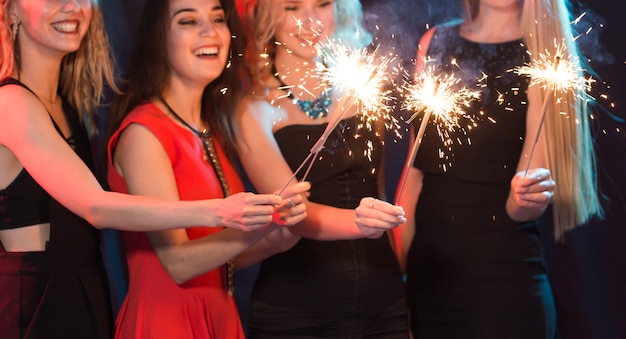 Celebrating with fun. Group of cheerful young women carrying sparklers. New year, holidays and party concept.