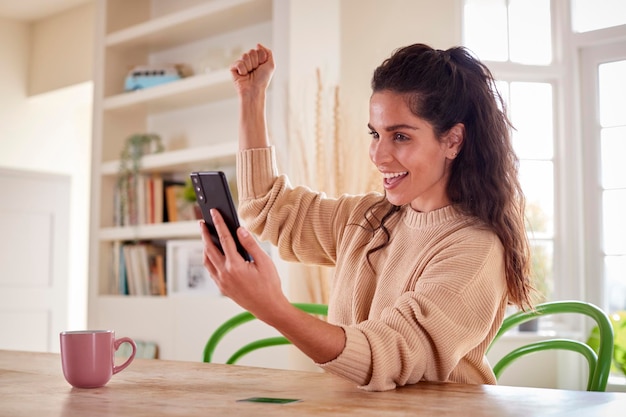 Foto celebrando la donna con la carta di credito a casa utilizzando il telefono cellulare per rivedere le finanze per avviare un'attività