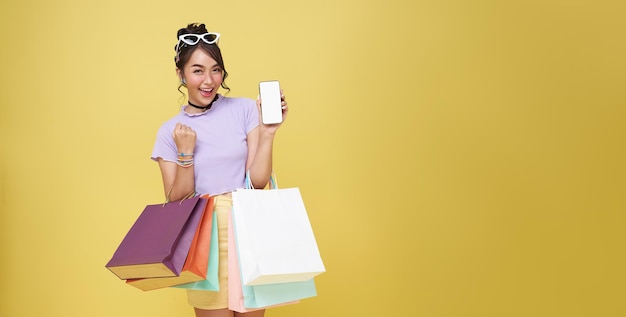 Празднование азиатской женщины улыбается, наслаждаясь покупками, она показывает смартфон, делающий покупки онлайн