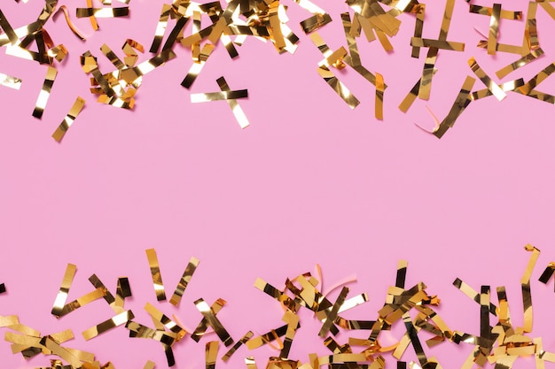 Celebration background with party gold confetti on pink background, copy space. Top view.