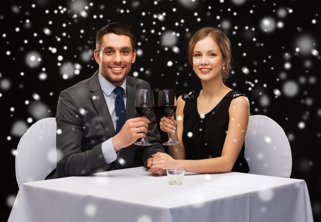 celebration, christmas, holidays and people concept - smiling couple clinking glasses of red wine at restaurant over black snowy background