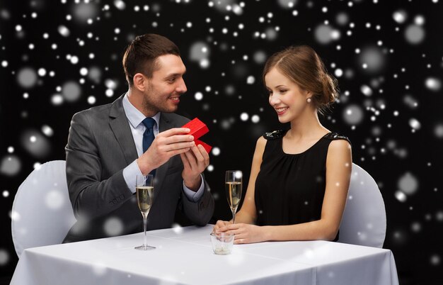 Celebrazione, natale, vacanze e concetto di persone - coppia sorridente con confezione regalo rossa al ristorante su sfondo nero innevato