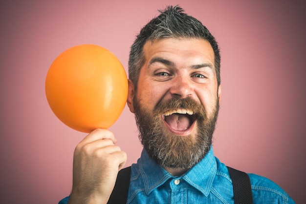 Celebration concept - happy bearded man holding air balloon in hands. Stylish man with beard and mustache in blue denim shirt holds balloon. Charming man in good mood. Emotions, feelings and reaction.