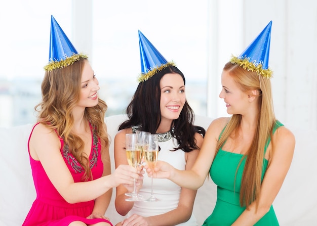 celebration, drinks, friends, bachelorette party, birthday concept - three smiling women wearing blue hats with champagne glasses