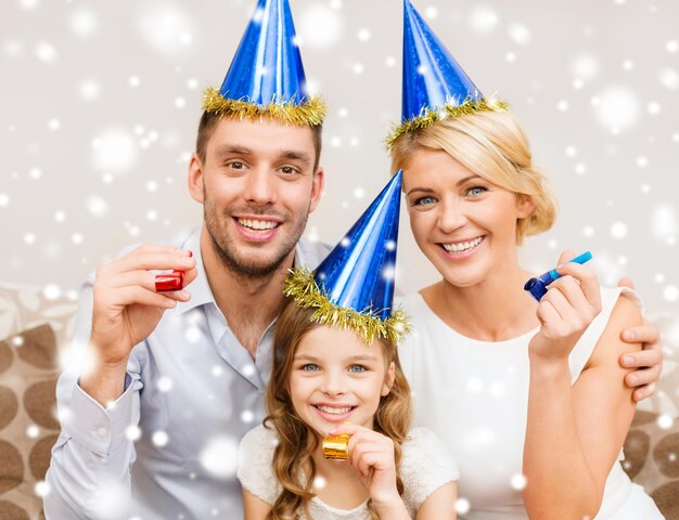 celebration, family, holidays and birthday concept - happy family wearing blue party hats and blowing favor horns at home