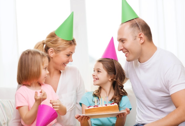 celebration, family, holidays and birthday concept - happy family with two kids in hats with cake at home