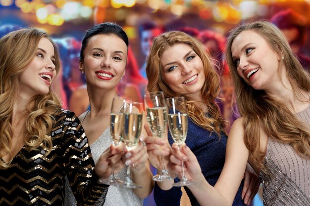 celebration, friends, bachelorette party and holidays concept - happy women clinking champagne glasses over nightclub lights background