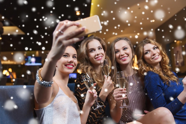 celebration, friends, bachelorette party, technology and holidays concept - happy women with champagne glasses and smartphone taking selfie at night club