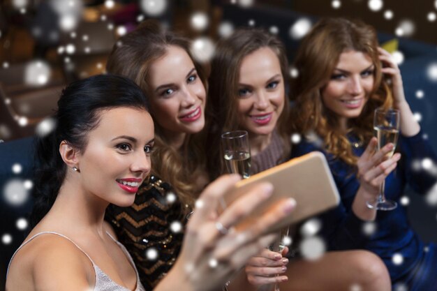 celebration, friends, bachelorette party, technology and holidays concept - happy women with champagne glasses and smartphone taking selfie at night club