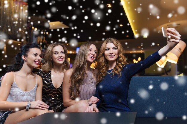 celebration, friends, bachelorette party, technology and holidays concept - happy women with smartphone taking selfie at night club