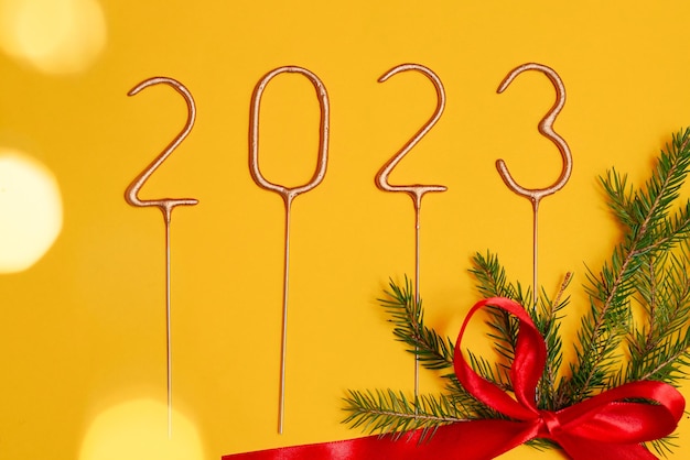 Фото Празднование нового 2023 года. цифры 2023 года выложены на желтом изолированном фоне с веткой елки и красным бантом. концепция зимних праздников и перемен года