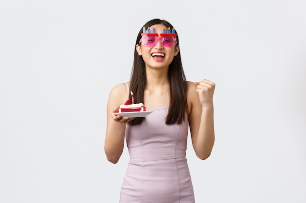 Celebration, party and holidays concept. Optimistic happy beautiful asian girl in funny glasses and dress, fist pump in triumph