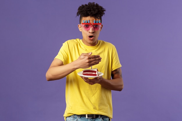 Celebration, party and holidays concept. Portrait of happy funny, enthusiastic young man celebrating birthday, protect lit candle on b-day cake from wind, making wish, smiling cheerful