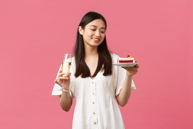 Celebrazione, feste di festa e concetto di divertimento. bella donna sognante che festeggia il suo compleanno con un bicchiere di champagne e una torta di b-day, sorridente spensierata al dessert, in piedi sfondo rosa.