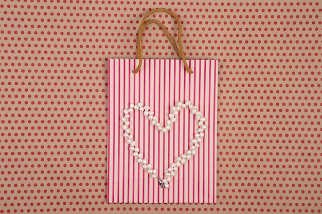 Celebratory concept handmade striped shopping bag of craft\
paper gift bags and women\'s pearl jewelry of heart