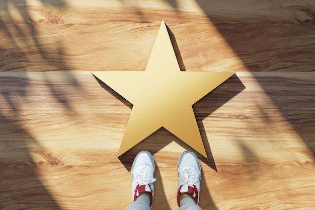 Celebrity popularity and fame concept with view from top on blank golden star with human feet in snickers on wooden surface mockup