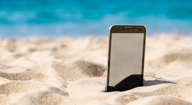 Сотовый телефон похоронен в песке красивого пляжа.
