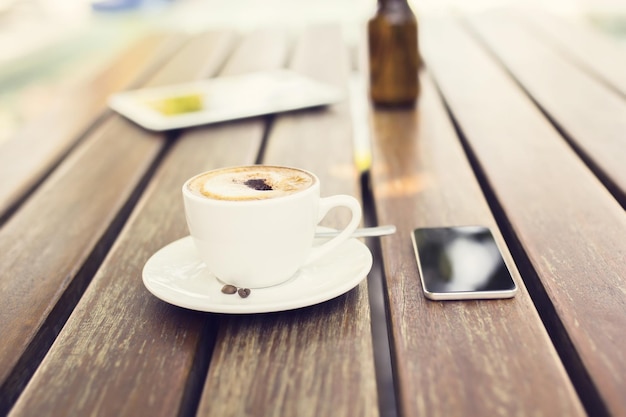 Cell phone and cup of coffee on a table outdoors