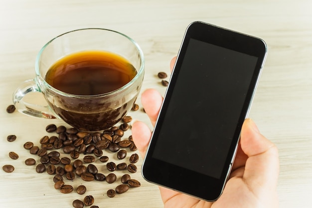 Cell phone in hand on the background of coffee