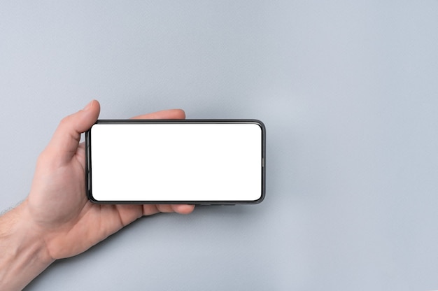 cell phone. male hand holding phone horizontally with blank white screen.