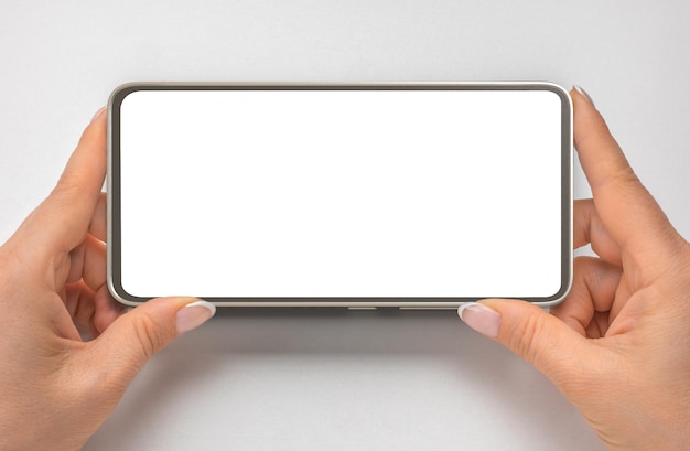 Photo cell phone mockup in horizontal position close up hands hold cellphone on gray background mobile phone with blank copy space screen for your text watching streaming video on phone