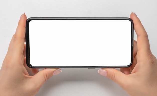 Cell phone mockup in horizontal position watching streaming video on phone close up hands hold cellphone whith blank screen on gray background Mobile phone with blank copy space screen for text