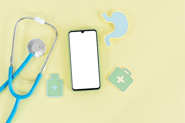 Cell phone with blank screen and stethoscope on yellow background Top view