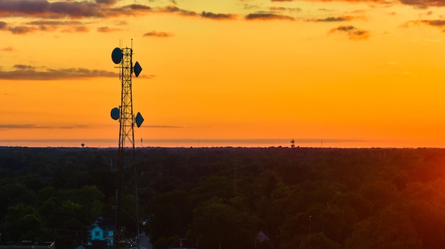 写真 緑色の森の上のセルタワーは ⁇ 黄色い空の夕暮れ時のアンテナで輝くオレンジ色です ⁇