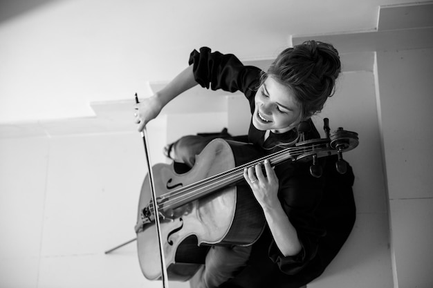 Cellist sits on the stairs and plays the cello and smiles enjoys performing music top view