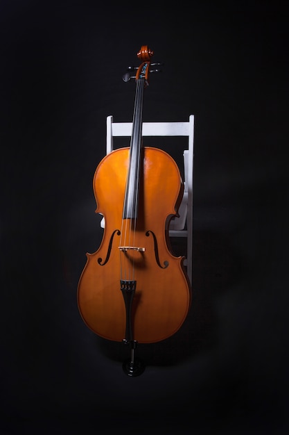 Cello leaning on white chair on black background