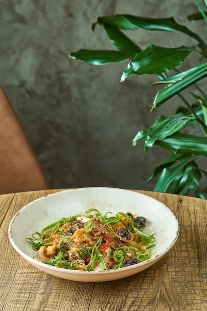 Tagliatelle di cellophane con gamberi e verdure, funghi shiitake in un piatto bianco. wok di spaghetti di riso