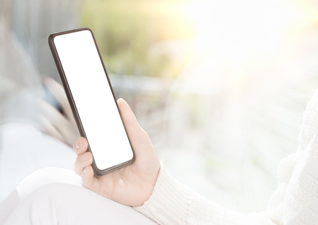 Cellphone mockup Girl sits by window and uses cell phone looks at smartphone reads shop communicates with friends in messenger bright light image