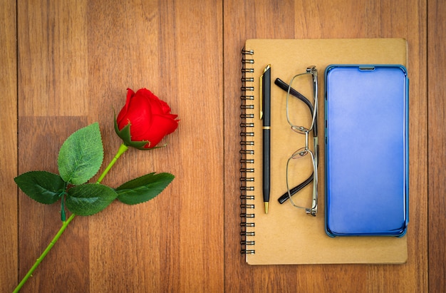 cellphone on notepad and red rose on wooden table