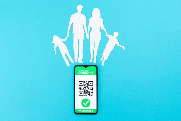 Cellulare con app di passaporto di immunità digitale e una silhouette di una famiglia ritagliata di carta su una parete blu. lay piatto. il concetto di vaccinazione e nuova normalità. copia spazio.