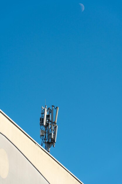 Антенна сотовой связи, установленная на крыше высотного здания на фоне голубого неба Телекоммуникационное оборудование радиосети 5G с радиомодулями и умными антеннами