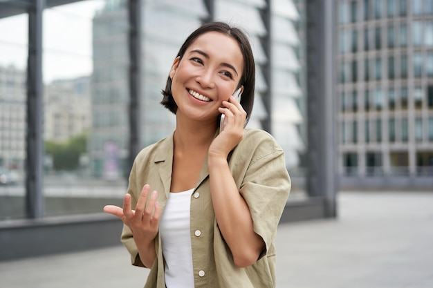 セルラー接続の若いアジア人女性は、携帯電話とウォーキングで電話をかけます