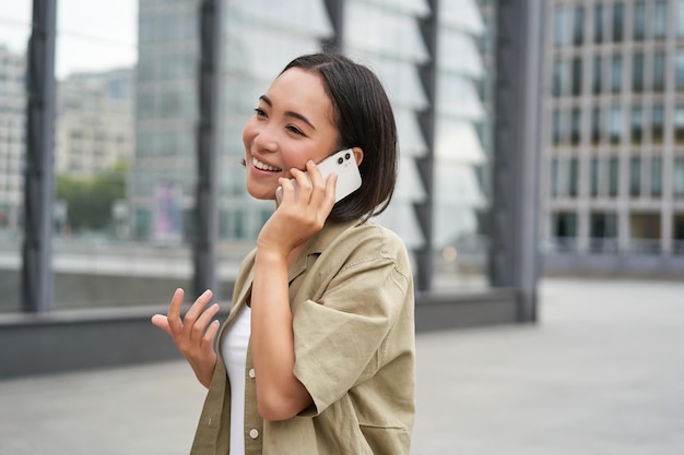 セルラー接続の若いアジア人女性は、携帯電話とウォーキングで電話をかけます