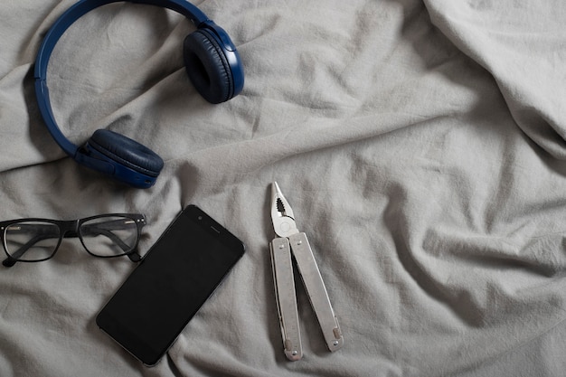 cellular phone glasses and multipurpose tool on bed with grey sheets