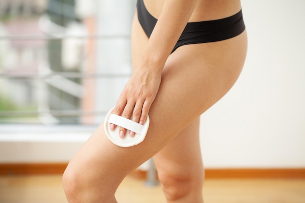 Cellulite treatment, woman arm holding dry brush to her leg.