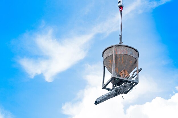 青い空を背景に建設現場でワイヤーにぶら下がっているセメントまたはコンクリートのバケツ