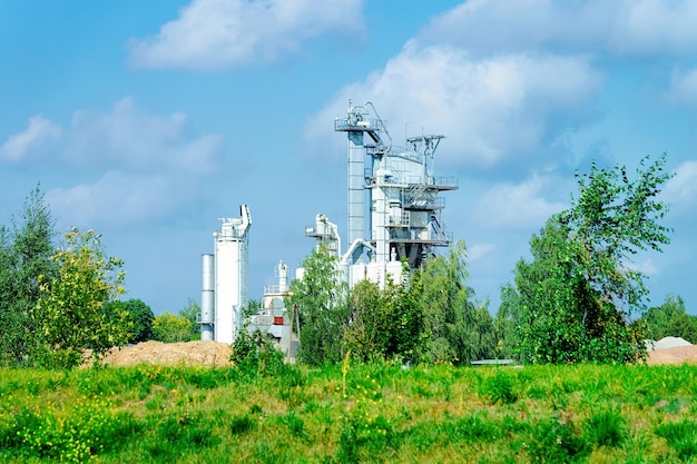 Cement plant and the green grass. Clouds in the blue sky.