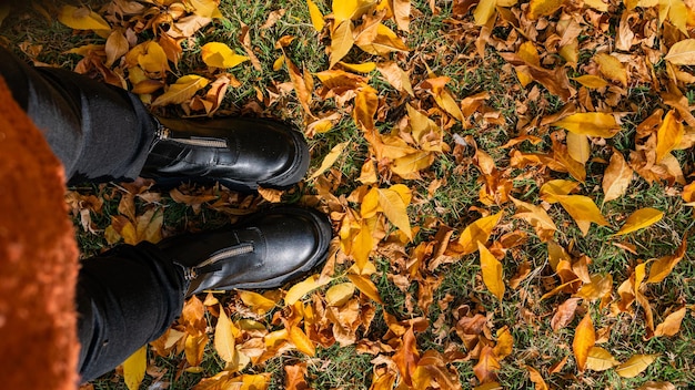 cenitale weergave vrouw voeten dragen zwarte laarzen staande op herfst oranje bladeren kopiëren ruimte