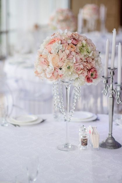 Centerpiece made of pink and white flowers stands in the middle of festive dinner table