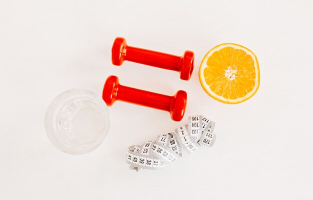 A centimeter, an orange, a glass of water and red dumbbells. Health care, diet and sport concept