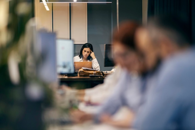 A CEO is sitting at her office and working while worker sitting in a blurry foreground