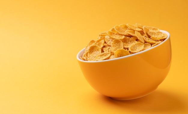 Ceramic bowl of corn flakes on yellow background with copy space